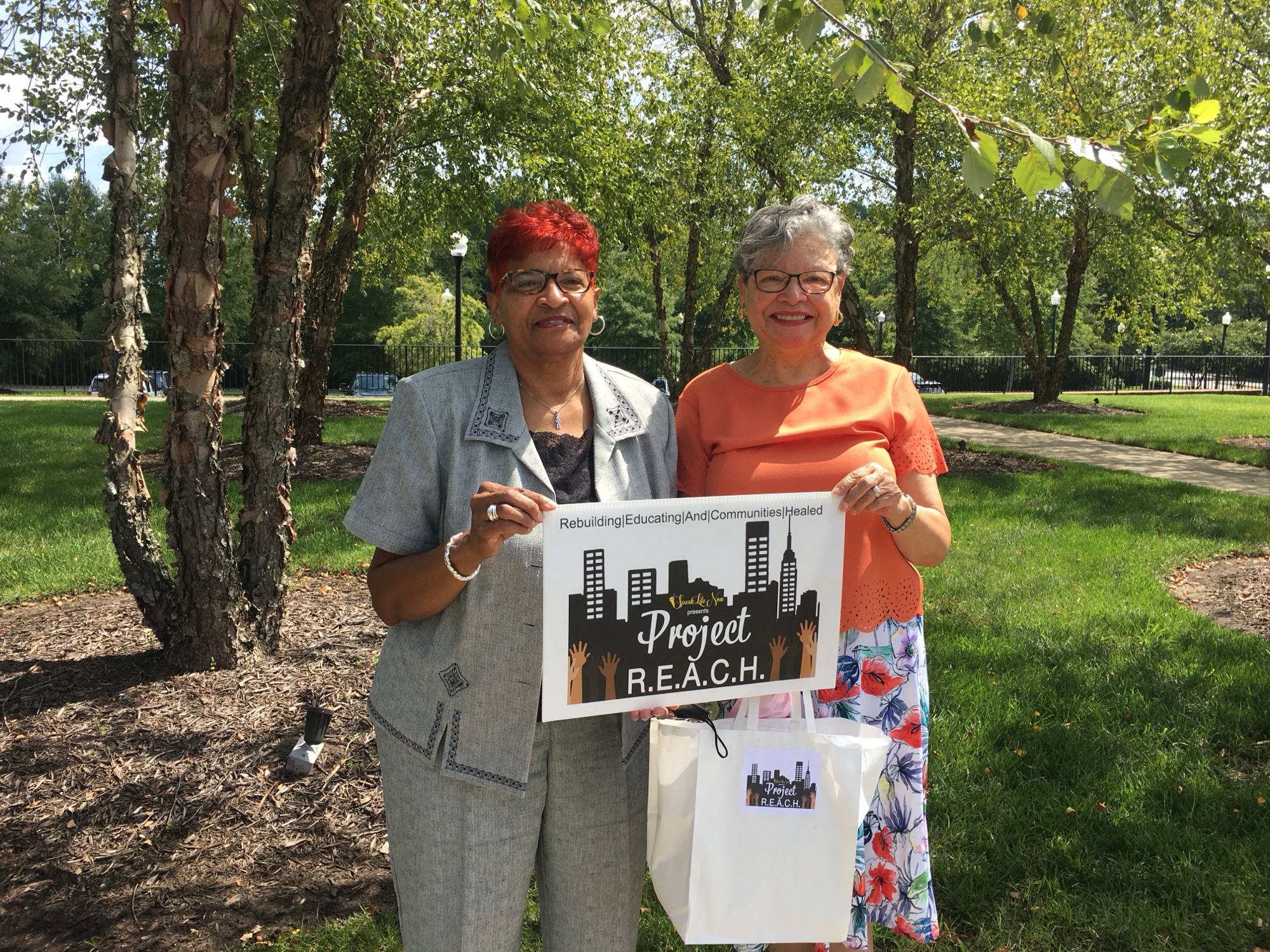 Two women holding a Project R.E.A.C.H. sign outdoors